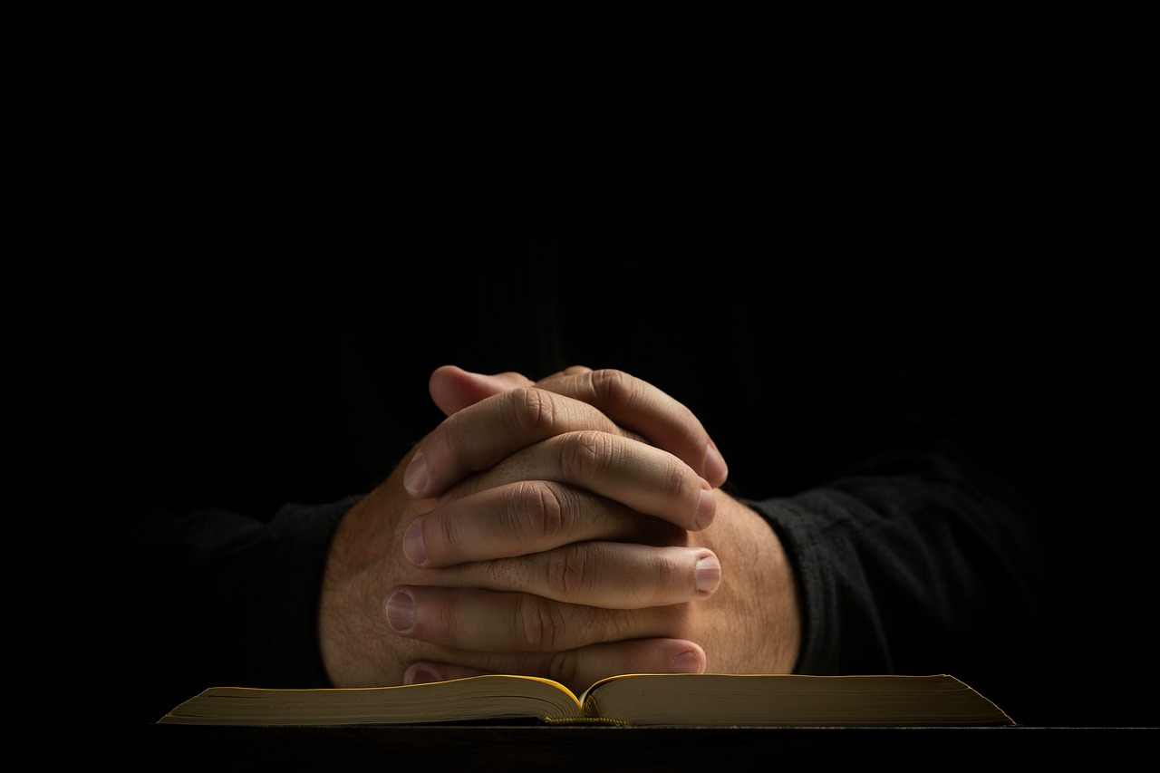 Hands clasped in prayer over a Bible