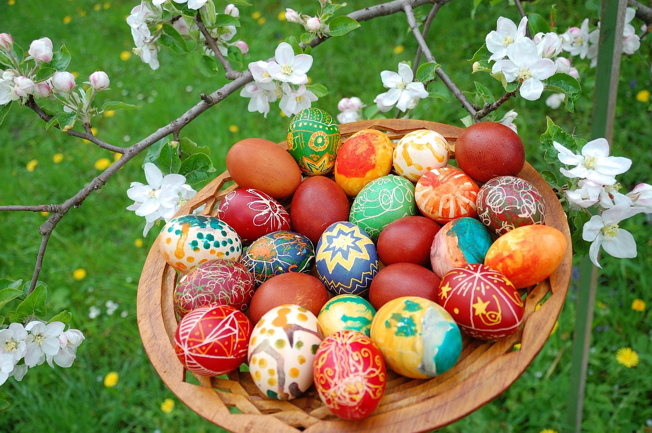 Painted Easter eggs on a plate in a garden by a tree with some white blossom.